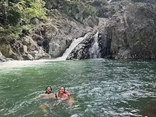 Due persone che nuotano in una piscina naturale tra le rocce ai piedi di una cascata