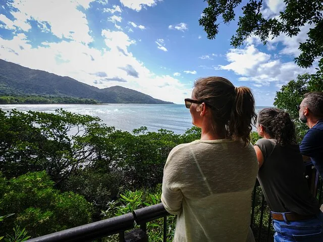 Turisti in piedi in un punto panoramico che si affaccia su una tranquilla baia oceanica e sulle montagne