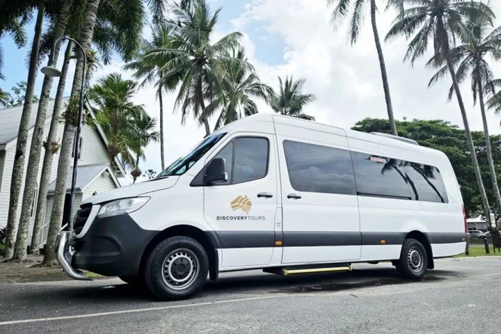 A white tour van parked on a street with palm trees and a white building in the background