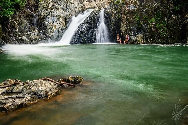 A wide view of a waterfall cascading into a green natural swimming hole